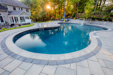Elegant backyard concrete paver and kidney-shaped pool landscaping photo in Boston