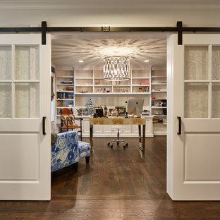 Inspiration för mellanstora klassiska hemmabibliotek, med mellanmörkt trägolv, ett fristående skrivbord, beige väggar och brunt golv