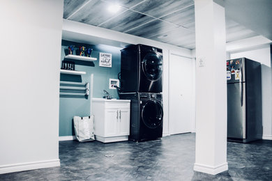 Example of a mid-sized minimalist vinyl floor, gray floor, vaulted ceiling and wall paneling utility room design in Toronto with a drop-in sink, white cabinets, multicolored walls and a stacked washer/dryer