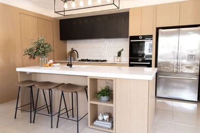 Photo of a mid-sized modern l-shaped open plan kitchen in Perth with a single-bowl sink, flat-panel cabinets, medium wood cabinets, quartz benchtops, white splashback, stone tile splashback, black appliances, porcelain floors, with island, beige floor and white benchtop.