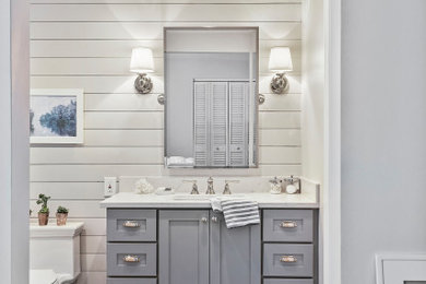 Inspiration for a mid-sized beach style master bathroom in Tampa with furniture-like cabinets, grey cabinets, an alcove shower, a one-piece toilet, white tile, subway tile, grey walls, porcelain floors, an undermount sink, engineered quartz benchtops, grey floor, a hinged shower door and white benchtops.