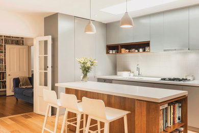 Contemporary kitchen in Sydney with an undermount sink, flat-panel cabinets, grey cabinets, white splashback, mosaic tile splashback, light hardwood floors, with island, beige floor and white benchtop.