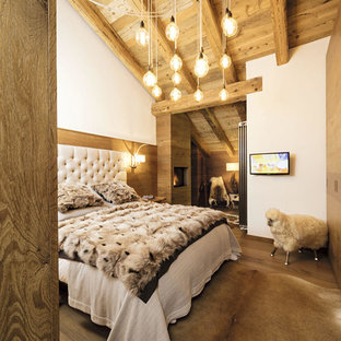 Foto på ett litet rustikt huvudsovrum, med vita väggar, mellanmörkt trägolv, brunt golv, en hängande öppen spis och en spiselkrans i trä