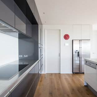 Réalisation d'une grande arrière-cuisine parallèle minimaliste avec un évier encastré, un placard à porte plane, des portes de placard grises, un plan de travail en inox, une crédence en carreau de miroir, un électroménager en acier inoxydable, sol en stratifié, un îlot central et un sol marron.