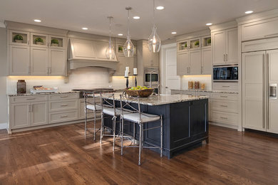 Mid-sized transitional l-shaped open plan kitchen in Seattle with a farmhouse sink, shaker cabinets, white cabinets, granite benchtops, stainless steel appliances, medium hardwood floors, with island, brown floor and brown benchtop.