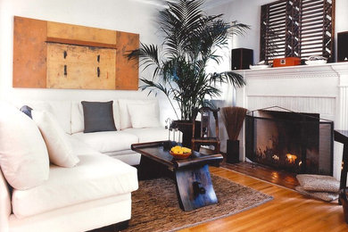 Inspiration for a mid-sized asian living room in Los Angeles with white walls, medium hardwood floors, a standard fireplace, a wood fireplace surround and no tv.