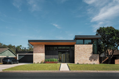 Large mid-century modern multicolored two-story brick and board and batten house exterior idea in Austin with a butterfly roof, a metal roof and a black roof