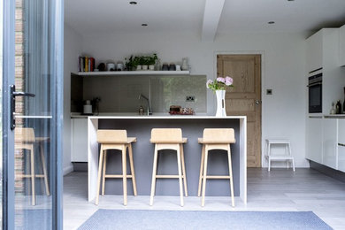 Photo of a mid-sized contemporary l-shaped open plan kitchen in Other with a single-bowl sink, white cabinets, quartzite benchtops, grey splashback, glass sheet splashback, black appliances, porcelain floors, with island, grey floor and grey benchtop.