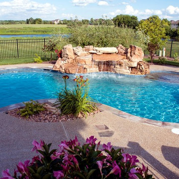 Free form pool with stone table, sun shelf, water feature, and outdoor kitchen,
