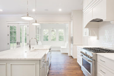Large transitional l-shaped open plan kitchen in Louisville with a farmhouse sink, shaker cabinets, white cabinets, marble benchtops, white splashback, subway tile splashback, stainless steel appliances, medium hardwood floors, with island and brown floor.