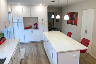 Inspiration for a mid-sized modern vinyl floor and brown floor kitchen remodel in Other with an undermount sink, flat-panel cabinets, white cabinets, quartz countertops, white backsplash, subway tile backsplash, white appliances, an island and white countertops