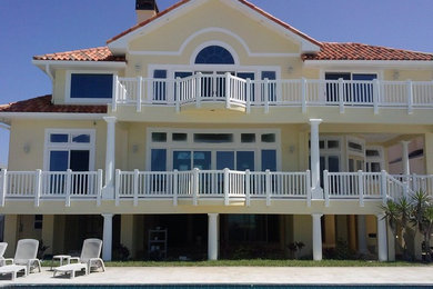 Inspiration for a large timeless yellow three-story stucco house exterior remodel in Tampa with a hip roof and a tile roof