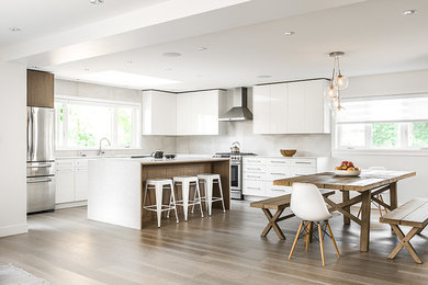 Mid-sized contemporary l-shaped open plan kitchen in Vancouver with flat-panel cabinets, white cabinets, quartz benchtops, stainless steel appliances, medium hardwood floors and with island.