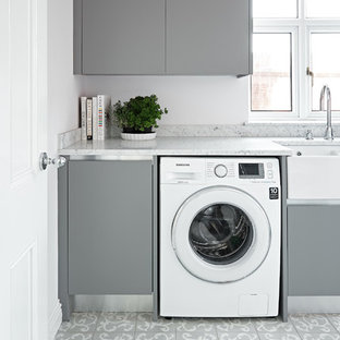 ウィルトシャーの小さいトランジショナルスタイルのおしゃれなランドリールーム (エプロンフロントシンク、フラットパネル扉のキャビネット、グレーのキャビネット、大理石カウンター、セラミックタイルの床、グレーの床) の写真