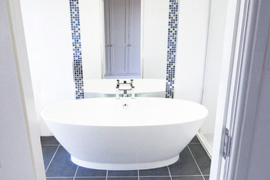 Expansive family bathroom in London with freestanding cabinets, black cabinets, a freestanding bath, a walk-in shower, a two-piece toilet, white tiles, white walls, porcelain flooring, a pedestal sink, grey floors and a hinged door.