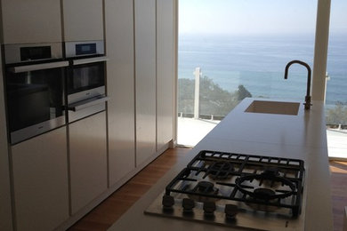 Example of a mid-sized minimalist galley light wood floor eat-in kitchen design in Los Angeles with a single-bowl sink, flat-panel cabinets, white cabinets and stainless steel appliances