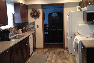 Inspiration for a timeless galley vinyl floor enclosed kitchen remodel in Other with a double-bowl sink, raised-panel cabinets, dark wood cabinets, quartz countertops, multicolored backsplash, glass tile backsplash, white appliances and no island