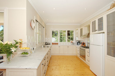 Inspiration for a mid-sized traditional u-shaped kitchen in Sydney with recessed-panel cabinets, beige cabinets, marble benchtops, beige splashback, ceramic splashback, stainless steel appliances, a single-bowl sink and light hardwood floors.