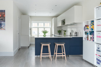 Inspiration for a mid-sized contemporary l-shaped eat-in kitchen in Berkshire with a double-bowl sink, flat-panel cabinets, blue cabinets, quartzite benchtops, white splashback, black appliances, a peninsula and white benchtop.