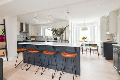 Inspiration for a large contemporary light wood floor and beige floor open concept kitchen remodel in Ottawa with a double-bowl sink, shaker cabinets, white cabinets, quartzite countertops, black backsplash, porcelain backsplash, stainless steel appliances, an island and white countertops