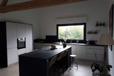 Aménagement d'une cuisine moderne avec des portes de placard blanches, un plan de travail en stratifié, une crédence noire, îlot, plan de travail noir et fenêtre au-dessus de l'évier.