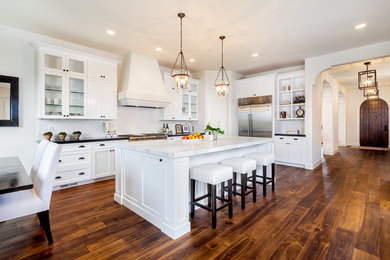 Eat-in kitchen - mediterranean l-shaped dark wood floor and brown floor eat-in kitchen idea in San Diego with recessed-panel cabinets, white cabinets, white backsplash, stainless steel appliances and an island