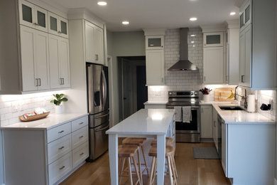 Large trendy u-shaped medium tone wood floor and brown floor eat-in kitchen photo in Other with an undermount sink, shaker cabinets, quartz countertops, white backsplash, ceramic backsplash, stainless steel appliances, an island, white countertops and white cabinets
