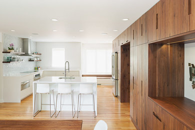 Design ideas for a large modern u-shaped eat-in kitchen in Philadelphia with an undermount sink, flat-panel cabinets, white splashback, stone tile splashback, stainless steel appliances, with island, brown floor, dark wood cabinets, solid surface benchtops, light hardwood floors and white benchtop.
