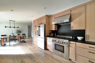 Eat-in kitchen - mid-sized 1960s galley light wood floor and beige floor eat-in kitchen idea in San Francisco with a farmhouse sink, shaker cabinets, light wood cabinets, granite countertops, black backsplash, stone slab backsplash, stainless steel appliances, a peninsula and black countertops