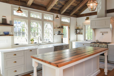 Example of a mid-sized transitional u-shaped medium tone wood floor, brown floor and exposed beam eat-in kitchen design in Other with a farmhouse sink, shaker cabinets, wood countertops, white backsplash, stainless steel appliances and white countertops