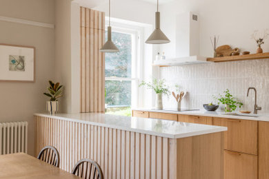 Classic u-shaped open plan kitchen in Other with a submerged sink, flat-panel cabinets, medium wood cabinets, engineered stone countertops, white splashback, a breakfast bar, grey floors and white worktops.