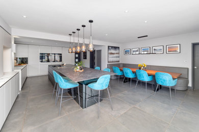 Large contemporary l-shaped kitchen/diner in Cheshire with flat-panel cabinets, white cabinets, white splashback, porcelain splashback, stainless steel appliances and an island.