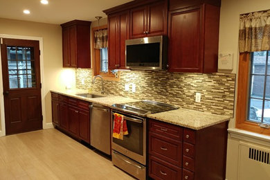 Mid-sized transitional galley light wood floor enclosed kitchen photo in Philadelphia with an undermount sink, raised-panel cabinets, dark wood cabinets, granite countertops, beige backsplash, matchstick tile backsplash, stainless steel appliances and no island