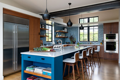シアトルにあるコンテンポラリースタイルのおしゃれなキッチン (アンダーカウンターシンク、フラットパネル扉のキャビネット、中間色木目調キャビネット、青いキッチンパネル、シルバーの調理設備、無垢フローリング、茶色い床、白いキッチンカウンター) の写真