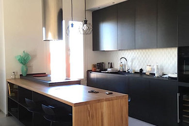 Idee per una grande cucina minimal con lavello integrato, ante lisce, ante nere, top in superficie solida, paraspruzzi bianco, paraspruzzi in gres porcellanato, elettrodomestici neri, pavimento in gres porcellanato, pavimento grigio, top nero e travi a vista