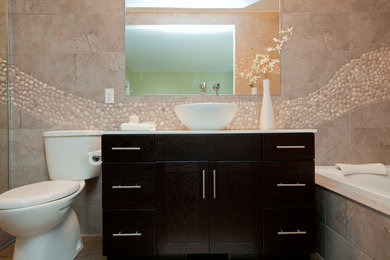 Mid-sized trendy master beige tile and stone tile dark wood floor alcove bathtub photo in Other with black cabinets, a one-piece toilet, a vessel sink, recessed-panel cabinets, beige walls and solid surface countertops