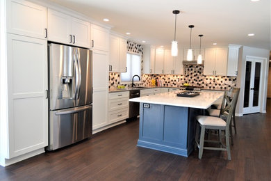 Large trendy l-shaped dark wood floor and brown floor eat-in kitchen photo in Milwaukee with a drop-in sink, shaker cabinets, white cabinets, solid surface countertops, multicolored backsplash, ceramic backsplash, stainless steel appliances and an island