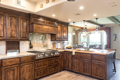 Kitchen - large traditional u-shaped ceramic tile and beige floor kitchen idea in Austin with an undermount sink, raised-panel cabinets, brown cabinets, granite countertops, beige backsplash, travertine backsplash, stainless steel appliances and a peninsula