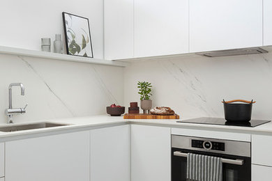 Modelo de cocinas en L actual con fregadero bajoencimera, armarios con paneles lisos, puertas de armario blancas, salpicadero blanco, salpicadero de losas de piedra, electrodomésticos de acero inoxidable, suelo multicolor y encimeras blancas
