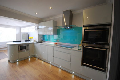 This is an example of a contemporary kitchen in Other with a built-in sink, flat-panel cabinets, white cabinets, quartz worktops, blue splashback, glass sheet splashback, integrated appliances, plywood flooring and a breakfast bar.