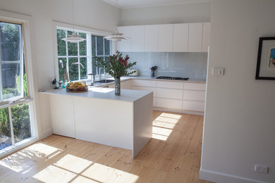 Inspiration for a mid-sized scandinavian u-shaped eat-in kitchen in Melbourne with flat-panel cabinets, white cabinets, a peninsula, an undermount sink, granite benchtops, white splashback, glass sheet splashback, light hardwood floors, stainless steel appliances and grey benchtop.