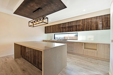 Photo of a large modern galley open plan kitchen in Melbourne with a double-bowl sink, beaded inset cabinets, dark wood cabinets, laminate benchtops, white splashback, ceramic splashback, painted wood floors, with island, beige floor and brown benchtop.