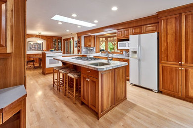 Photo of a large traditional l-shaped eat-in kitchen in Other with a double-bowl sink, raised-panel cabinets, medium wood cabinets, grey splashback, white appliances, light hardwood floors, with island and brown floor.