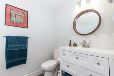 Small transitional white tile and marble tile gray floor and single-sink bathroom photo in Other with shaker cabinets, white cabinets, a two-piece toilet, gray walls, an integrated sink, solid surface countertops, white countertops and a freestanding vanity