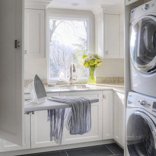 トロントの中サイズのトランジショナルスタイルのおしゃれな洗濯室 (上下配置の洗濯機・乾燥機、白いキャビネット、アンダーカウンターシンク、落し込みパネル扉のキャビネット、御影石カウンター、スレートの床、ベージュのキッチンカウンター) の写真