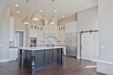 Inspiration for a transitional medium tone wood floor kitchen remodel in Other with a farmhouse sink, white cabinets, quartz countertops, white backsplash, ceramic backsplash, stainless steel appliances, an island and white countertops