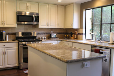 Inspiration for a mid-sized timeless l-shaped dark wood floor and brown floor enclosed kitchen remodel in San Luis Obispo with an undermount sink, raised-panel cabinets, white cabinets, quartz countertops, beige backsplash, stone tile backsplash, stainless steel appliances and an island