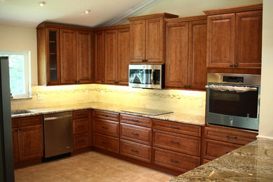Kitchen - mid-sized traditional u-shaped porcelain tile and brown floor kitchen idea in Miami with an undermount sink, raised-panel cabinets, medium tone wood cabinets, granite countertops, beige backsplash, stone tile backsplash, stainless steel appliances and an island