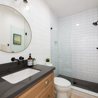 Photo of a transitional 3/4 bathroom in Orange County with shaker cabinets, medium wood cabinets, an alcove shower, a two-piece toilet, subway tile, white walls, wood-look tile, an undermount sink, engineered quartz benchtops, brown floor, a hinged shower door, black benchtops, a single vanity, a built-in vanity and planked wall panelling.