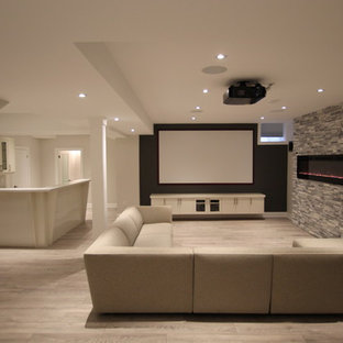 This is an example of a large contemporary look-out basement in Toronto with grey walls, laminate floors, a ribbon fireplace, a stone fireplace surround and grey floors.